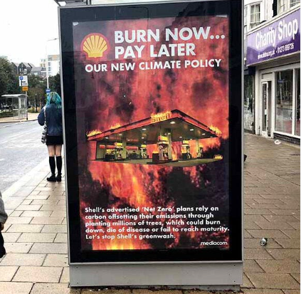 A bus stop with a fake Shell advert. The advert shows a petrol station on fire with the title 'Burn Now... Pay Later, our new climate policy