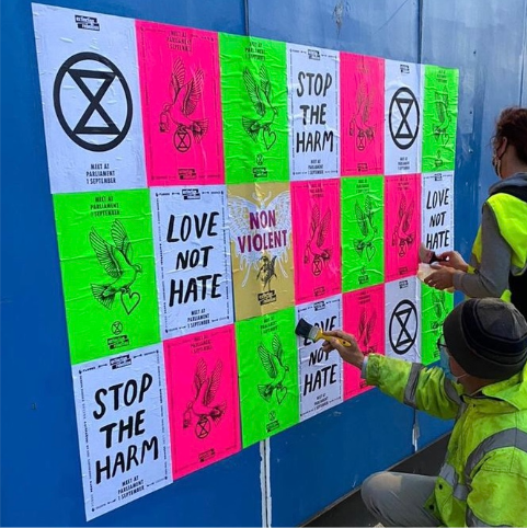 a grid of assorted XR posters if being pasted onto a bluw wall by two people wearing hi-vis jackets