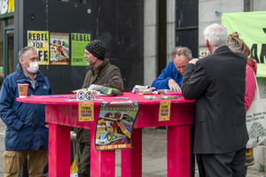 5 people stand and talk around a large pink table adorned with XR posters and Citizens Assembly leaflets