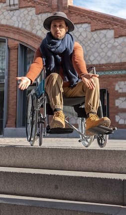 person in wheelchair at the top of a set of steps. Their arms are outstretched with palms up