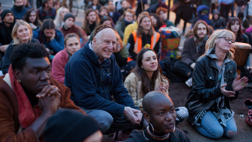 Rebels listen, some smiling and clapping, to a speaker or performer out of picture