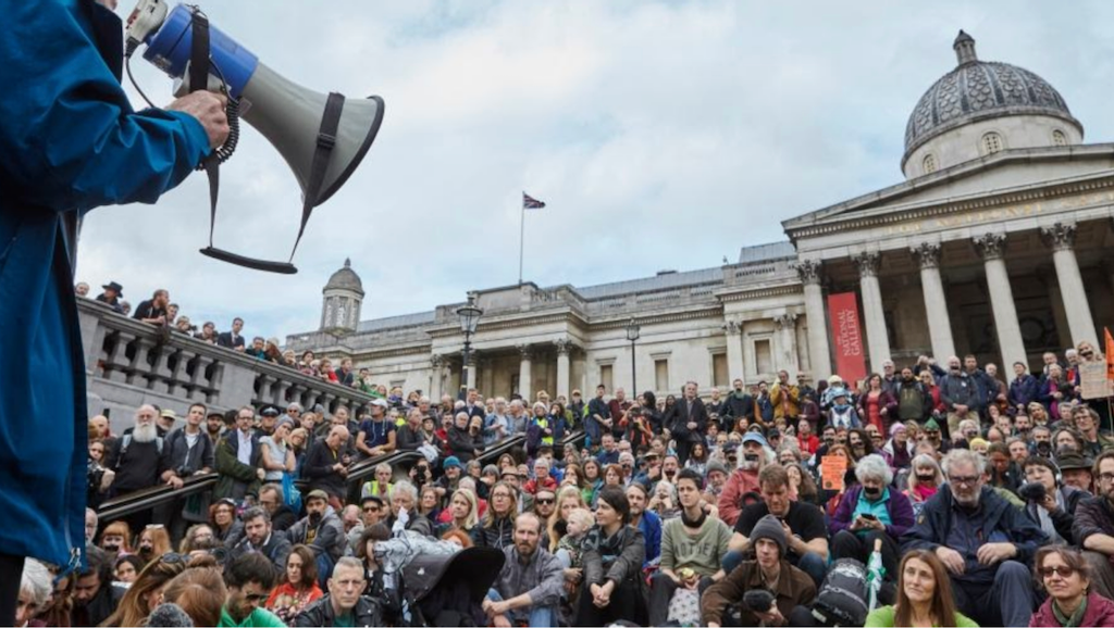 a speaker with a loud hailer addresses a large gathering of rebels on hte steps of Trafalgar Square, London